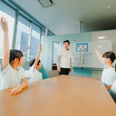 教室で手を挙げる子どもたちとスタッフ