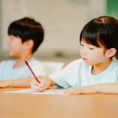 机に向かって鉛筆で書く子どもたち